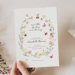 May include: A baby shower invitation with a floral wreath design. The invitation features the text "our little Lovebug is on the way" and details for the event, including the name "Elizabeth Thomas" and the date. Butterflies and flowers decorate the invitation.