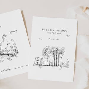 Puede incluir: Dos libros para bebés ilustrados en blanco y negro. Un libro presenta un ganso en un carro de madera, el otro libro se titula "Baby Harrison's First ABC Book" con animales del bosque y mariposas. Las palabras "Made with Love" también están en el libro.
