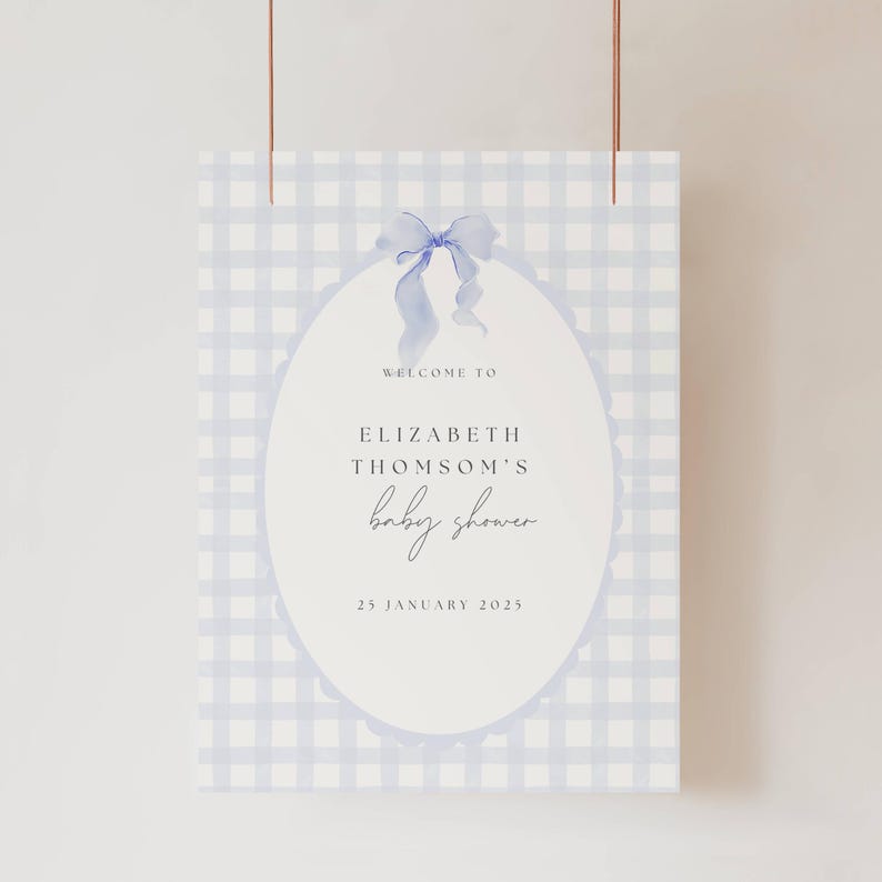 May include: A baby shower sign with a blue gingham pattern background. The sign features an oval shape with the words "Welcome to Elizabeth Thomson's baby shower" and the date "25 January 2025". A blue bow is at the top.