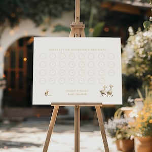Peut inclure: Un panneau de baby shower crème sur un chevalet en bois. Le panneau porte l'inscription "Devinez la date d'accouchement du petit caneton" et "BABY SHOWER d'Elizabeth & Marcus". Il présente des illustrations de canards et des cercles.