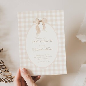 May include: A baby shower invitation with a beige gingham pattern. The invitation has an oval design with a watercolour bow and the text "BABY SHOWER" and details for Elizabeth Thomas.