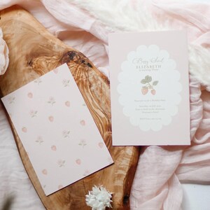 May include: A light pink birthday invitation card and a matching patterned card featuring small strawberries and flowers. The invitation has a scalloped white center frame with the text Berry Sweet ELIZABETH is turning Three and event details.
