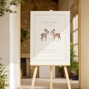 Puede incluir: Un letrero blanco sobre un caballete de madera con el texto "buck or doe? let's find out." Dos ilustraciones de ciervos con lazos azules y rosas están encima del texto. El letrero dice "Welcome to Elizabeth & Marcus's Gender Reveal Party."