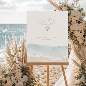 May include: A beach-themed bridal shower sign on an easel. The sign reads "Seashells & Wedding Bells" and "Welcome to Elizabeth Thomas's bridal shower." The sign features a watercolor design of a beach scene with a seashell graphic.