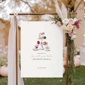 May include: A sign for a tea party, with a watercolour illustration of a tiered cake stand, teacups, and the text "Tea with mom-to-be Elizabeth Thomas". The sign is decorated with flowers and ribbons, perfect for a baby shower.