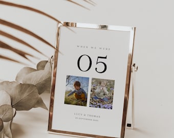 Puede incluir: Una tarjeta de número de mesa blanca con un marco dorado y un soporte. La tarjeta tiene el texto "When we were 05" y dos fotos de niños. El texto "Lucy & Thomas 25 September 2021" está en la parte inferior de la tarjeta.