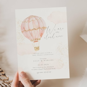 May include: A baby shower invitation featuring a pink hot air balloon with gold accents and the phrase "We are on cloud nine." The invitation includes details for the event, such as the date, time, location, and honorees, Lucy & Marchs.