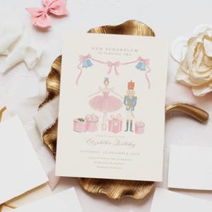 May include: A cream-colored birthday invitation card featuring a watercolor illustration of a ballerina and a nutcracker surrounded by pink gifts, blue bells, and ribbons. The text reads Our Sugarplum is turning two, Please join us for Elizabeth's Birthday, Saturday, 25 December 202X, four o'clock in the afternoon, Harrison's Residence, Manhattan Road.