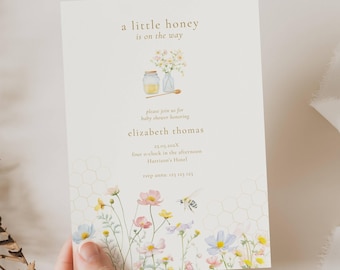 May include: Baby shower invitation with floral and honeycomb design. The invitation reads "a little honey is on the way" and includes details for Elizabeth Thomas's baby shower. Features watercolor illustrations of flowers, honey, and a bee.