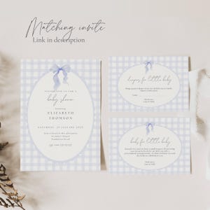 May include: Baby shower invitation set with a light blue gingham pattern. The main invitation features an oval frame with a blue bow and the text "baby shower" and details for Elizabeth Thomson. Includes inserts for diapers and books.