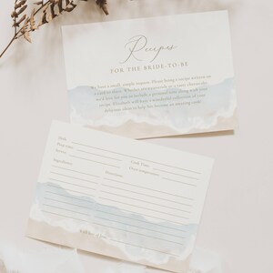 May include: Two recipe cards for a bride-to-be, featuring a watercolour design with light blue and beige tones, reminiscent of a beach. The top card displays the word "Recipes" in elegant script. The bottom card has recipe detail lines.