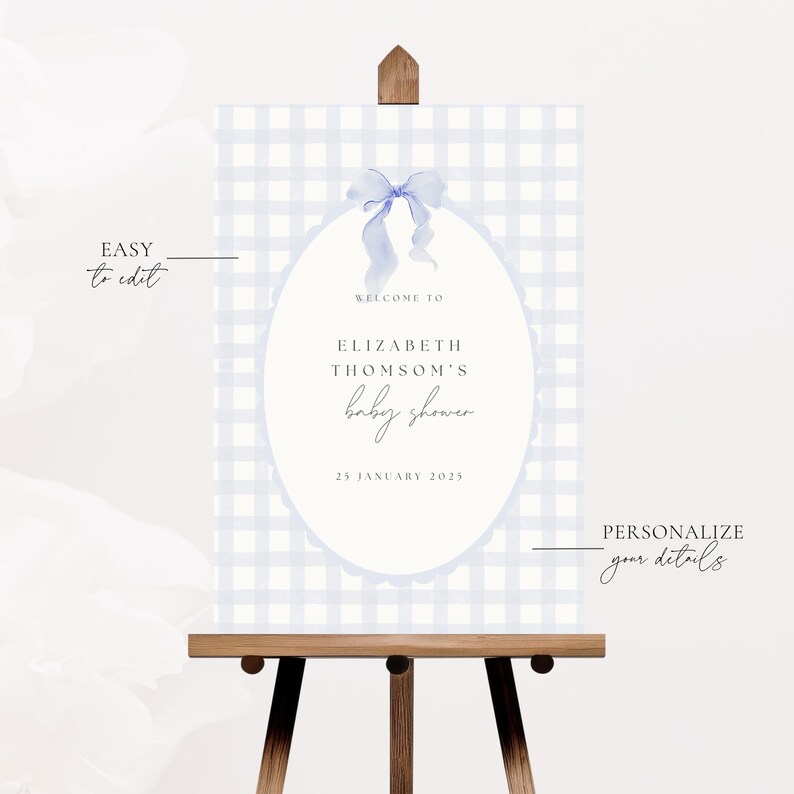 May include: A baby shower sign on a wooden easel. The sign has a light blue gingham pattern background with an oval in the center. The oval contains the text "WELCOME TO ELIZABETH THOMSON'S baby shower" and the date "25 JANUARY 2025".