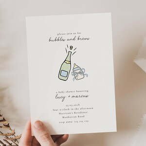 以下が含まれることがあります： 「bubbles and brews」の文字が入った、クリーム色のベビーシャワー招待状。シャンパンボトルと哺乳瓶のイラストが特徴です。ルーシーとマーカスへの招待状で、日付、時間、場所が記載されています。