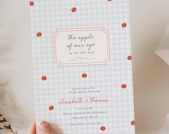 May include: Baby shower invitation with a light blue gingham pattern and red apple illustrations. The text reads "the apple of our eye is on the way" in a decorative frame. Additional text includes names, date, time, and location.