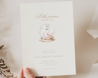 May include: Cream-colored baby shower invitation with gold text and a watercolor illustration of a swan in a snow globe. The text reads "A little princess is on the way" and includes event details.