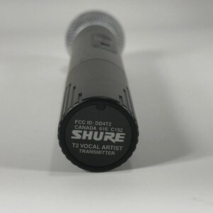 Puede incluir: Un micr&oacute;fono Shure T2 Vocal Artist Transmitter gris. El micr&oacute;fono tiene una cabeza de malla plateada y un cuerpo gris oscuro. La parte inferior del micr&oacute;fono tiene el logotipo de Shure y el texto "T2 Vocal Artist Transmitter".
