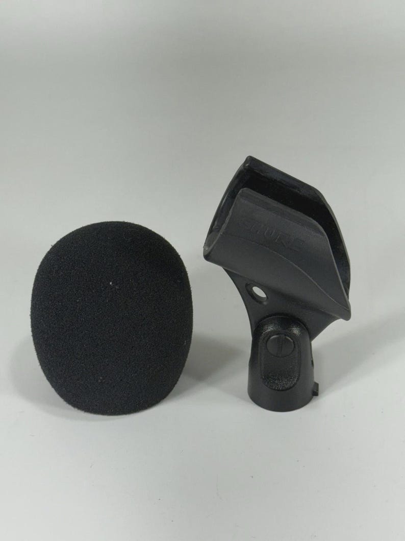 Puede incluir: Un filtro antipop negro y un soporte negro para micr&oacute;fono. El filtro antipop tiene forma ovalada y redondeada, hecho de un material poroso. El soporte es de pl&aacute;stico duro y tiene la marca "SHURE".
