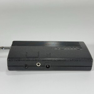 Puede incluir: Un dispositivo de audio negro Shure con un cable adjunto. El dispositivo tiene varios conectores de entrada y el logotipo de Shure. El dispositivo es rectangular y tiene una superficie texturizada.