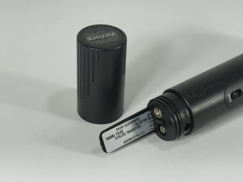 Puede incluir: Transmisor de micr&oacute;fono inal&aacute;mbrico Shure T2-CE negro con un compartimento de bater&iacute;a cil&iacute;ndrico negro y una tapa negra separada. El transmisor tiene una etiqueta que dice "MODEL T2-CE WIRELESS TRANSMITTER ASSEMBLED IN U.S.A."
