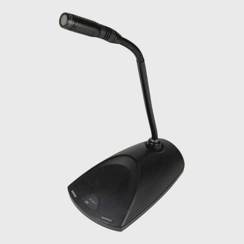 May include: A black desktop gooseneck microphone featuring a flexible neck and a base with a push button. The base displays the text PUSH and MICROFLEX. The microphone head is cylindrical with a mesh grille, designed for clear audio capture.