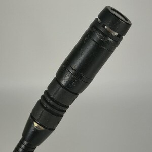 May include: A black cylindrical microphone with a metallic mesh top and a ribbed handle section. The microphone body shows signs of wear with minor paint chips and a textured finish, attached to a flexible gooseneck stand at the base.