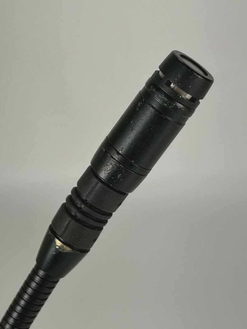May include: A black cylindrical microphone with a metallic mesh top and a ribbed handle section. The microphone body shows signs of wear with minor paint chips and a textured finish, attached to a flexible gooseneck stand at the base.