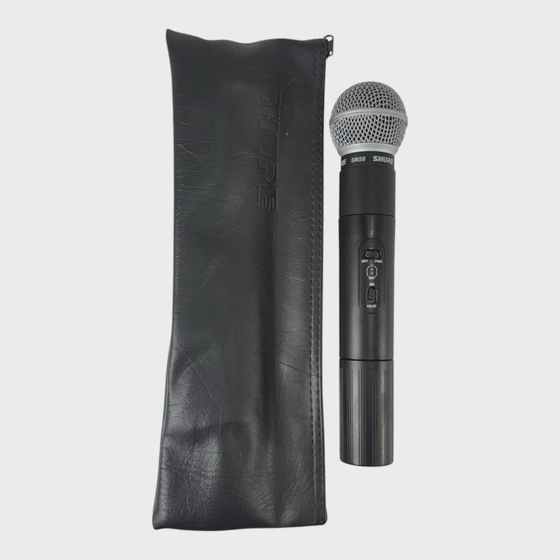 May include: A black Shure SM58 microphone with a silver mesh head, next to a black leather carrying case. The microphone has control buttons and a ribbed base. The case has the brand name printed on it.