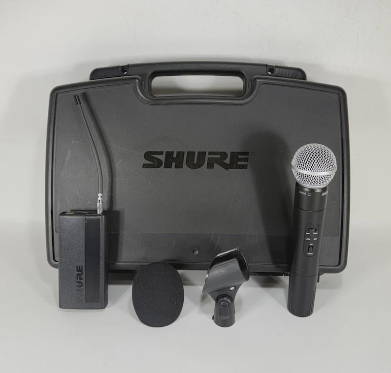 Puede incluir: Un sistema de micr&oacute;fono inal&aacute;mbrico Shure negro con un estuche de transporte. El juego incluye un micr&oacute;fono de mano, un receptor, un clip para micr&oacute;fono y un parabrisas. El logotipo de Shure es visible en el estuche y el receptor.