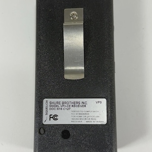 Puede incluir: Un receptor negro Shure Brothers Inc. VP3-CE con un clip met&aacute;lico y antena. El receptor tiene una etiqueta con texto que incluye "FCC STANDARDS" y "MADE IN TAIWAN".