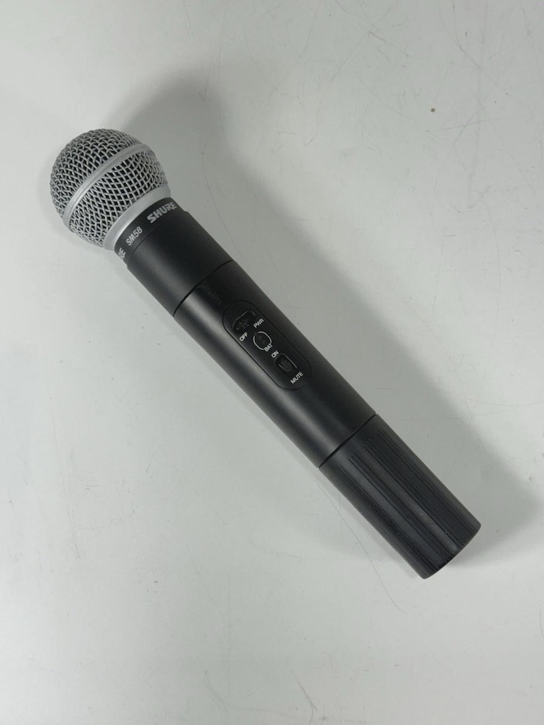 May include: A black Shure SM58 microphone with a silver mesh head. The microphone has a cylindrical body with an on/off switch and a mute button. The microphone is designed for vocal performances and recording.
