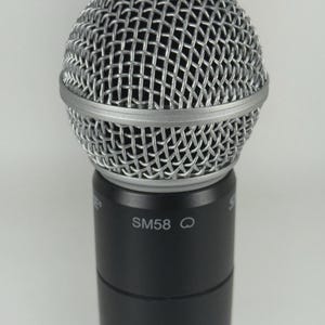 Puede incluir: Primer plano de un micr&oacute;fono plateado con una cabeza de malla y una base negra. El texto "SM58" est&aacute; impreso en la base del micr&oacute;fono. El micr&oacute;fono est&aacute; dise&ntilde;ado para actuaciones vocales y grabaci&oacute;n.