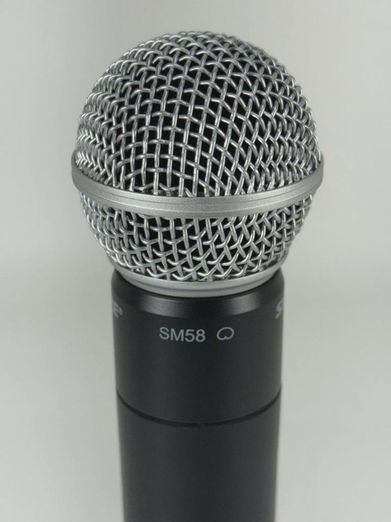 Puede incluir: Primer plano de un micr&oacute;fono plateado con una cabeza de malla y una base negra. El texto "SM58" est&aacute; impreso en la base del micr&oacute;fono. El micr&oacute;fono est&aacute; dise&ntilde;ado para actuaciones vocales y grabaci&oacute;n.