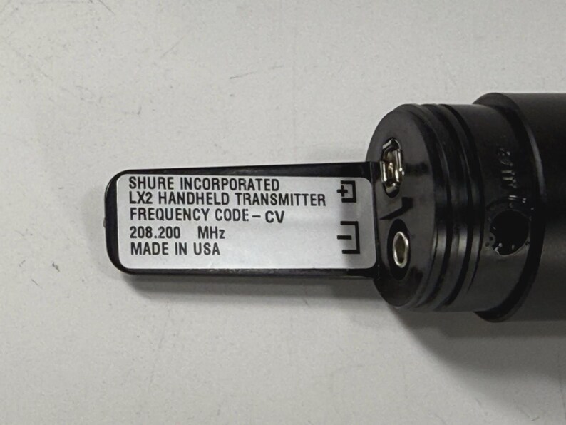 May include: A black Shure LX2 handheld transmitter with a label that reads "Shure Incorporated, LX2 Handheld Transmitter, Frequency Code-CV, 208.200 MHz, Made in USA."