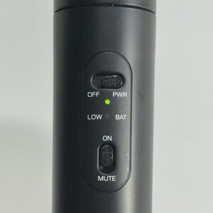 Puede incluir: Primer plano de un micr&oacute;fono negro con botones de control. Los botones incluyen "OFF", "PWR", "LOW", "BAT", "ON" y "MUTE". Una luz verde indica la alimentaci&oacute;n. El micr&oacute;fono es cil&iacute;ndrico.