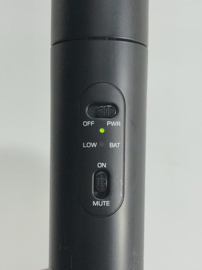 Puede incluir: Primer plano de un micr&oacute;fono negro con botones de control. Los botones incluyen "OFF", "PWR", "LOW", "BAT", "ON" y "MUTE". Una luz verde indica la alimentaci&oacute;n. El micr&oacute;fono es cil&iacute;ndrico.