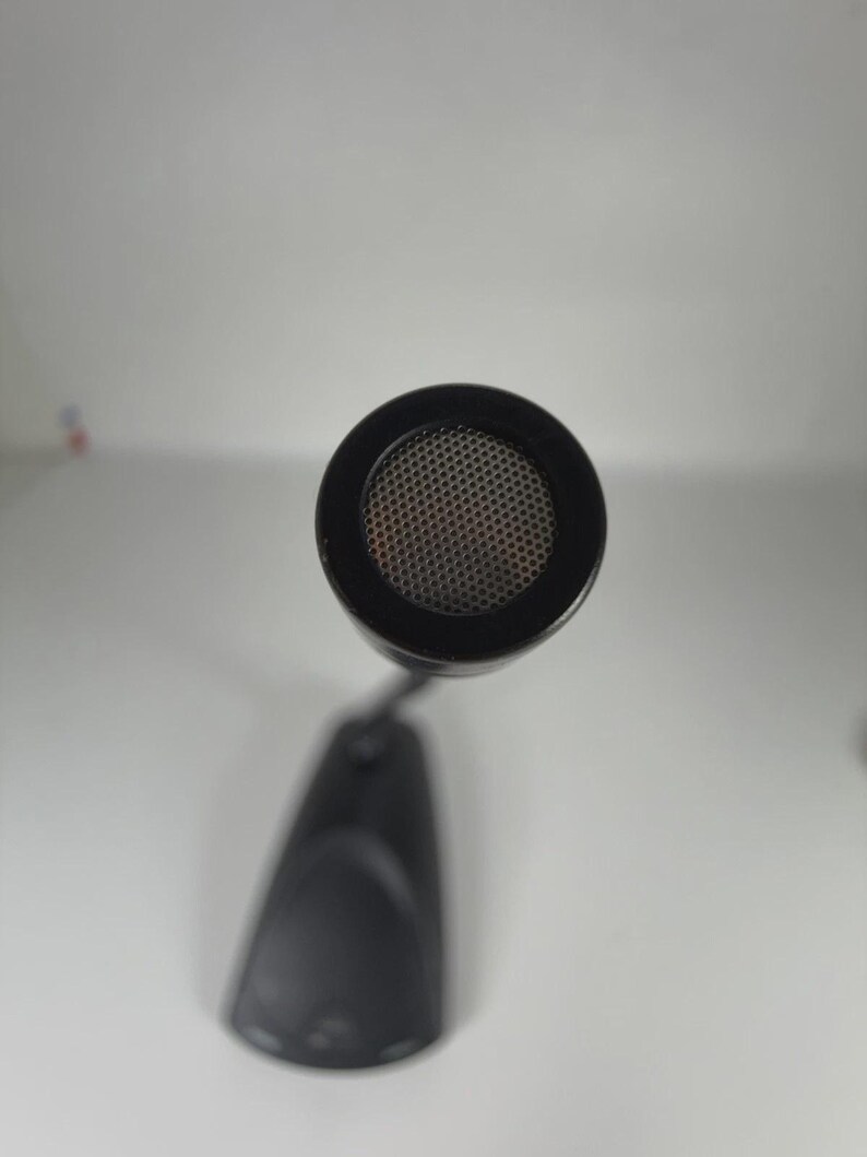 May include: A black gooseneck microphone featuring a circular head with a fine metal mesh grille. The microphone is attached to a solid, tapered black base that sits flat. The view is from directly above, highlighting the circular mesh pattern.