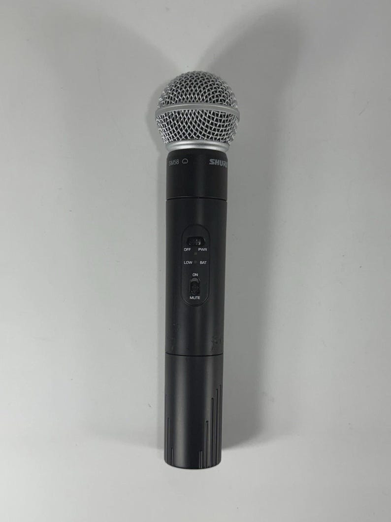 Puede incluir: Un micr&oacute;fono inal&aacute;mbrico negro con una cabeza de malla plateada. El micr&oacute;fono tiene un cuerpo cil&iacute;ndrico con botones de control y la marca "Shure" visible. El micr&oacute;fono est&aacute; dise&ntilde;ado para aplicaciones de audio profesionales.