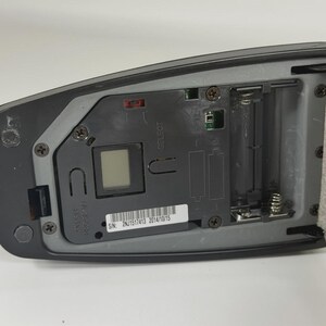 May include: A black electronic device with an open battery compartment, a small square digital display, and a white label featuring the serial number 2NJ1517413 2014/10/15. The internal grey plastic housing includes metal springs and screws.