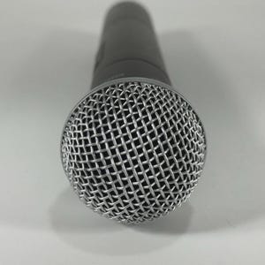 Puede incluir: Primer plano de un micr&oacute;fono gris oscuro. El micr&oacute;fono tiene una cabeza de malla plateada y un cuerpo cil&iacute;ndrico. La cabeza de malla est&aacute; hecha de un metal fino e entrelazado. El micr&oacute;fono est&aacute; dise&ntilde;ado para grabaci&oacute;n vocal o instrumental.