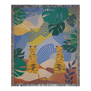 May include: Woven throw blanket featuring a vibrant jungle scene with two tigers. The design includes yellow, green, blue, and brown hues, with a fringed edge. The tigers are yellow with black stripes, and the background has abstract shapes.