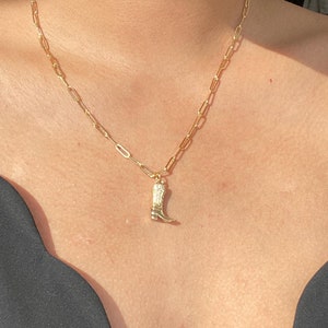 Könnte beinhalten: Eine goldene Kettenkette mit einem goldenen Stiefel-Anhänger. Die Kette besteht aus kleinen, miteinander verbundenen Ovalen.
