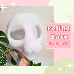 May include: A white feline base with large eye openings and a textured surface. The text "Feline Base" and "Flexible TPU" are displayed on a pink background. A hand holds a green plant in the foreground.