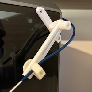 May include: White plastic 3D printed cable management arm with a blue cable attached. The arm is mounted to a black surface and has a gear and a knob.