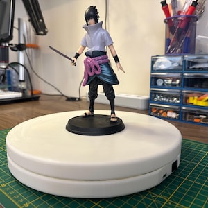 May include: A white rotating turntable with a black base. A black-haired anime figure with a purple sash and a sword is standing on the turntable.