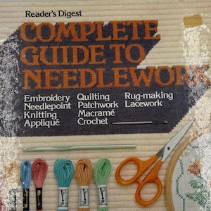 May include: A vintage "Reader's Digest Complete Guide to Needlework" book. The cover features the title in orange and white, with a list of needlework techniques.  Scissors, embroidery floss, and needles are also visible.