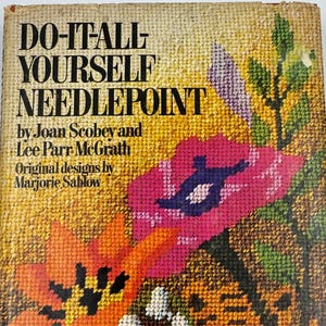 May include: A vintage book titled "DO-IT-ALL YOURSELF NEEDLEPOINT" with a colorful needlepoint floral design on the cover. The cover features orange and pink flowers, a tiger, and the names of the authors and designer.