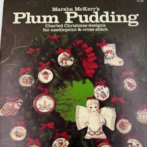 May include: A vintage book cover titled "Plum Pudding" by Marsha McKerr's. The cover features a Christmas wreath with ornaments, bows, and an angel. The book is for charted Christmas designs for needlepoint and cross stitch.
