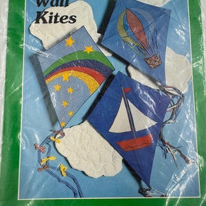 May include: A green-bordered package with the text "A Patchwork Pattern and Instructions by Yours Truly" and "Wall Kites." The package shows three kite designs: a hot air balloon, a sailboat, and a kite with stars and rainbows. Finished kite size is approximately 20" x 26".