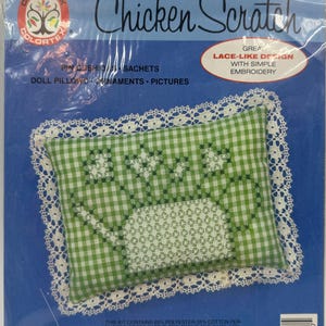 May include: A Colortex Chicken Scratch craft kit in a clear plastic bag. The package features a green and white gingham pillow with white lace trim and embroidery. Text includes Chicken Scratch, Pin Cushions, Sachets, Doll Pillows, Ornaments, Pictures, and Great Lace-Like Design With Simple Embroidery.