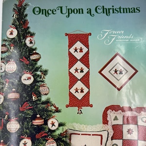 Pode incluir: Uma capa de livro vintage com tema natalino com o título "Once Upon a Christmas". A capa apresenta uma árvore de Natal decorada, ornamentos e desenhos de ponto cruz com detalhes em vermelho e branco. Uma variedade de decorações de Natal são exibidas.